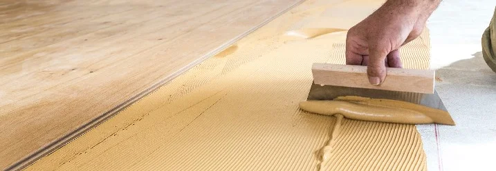Person verteilt Kleber mit Spachtel auf Boden